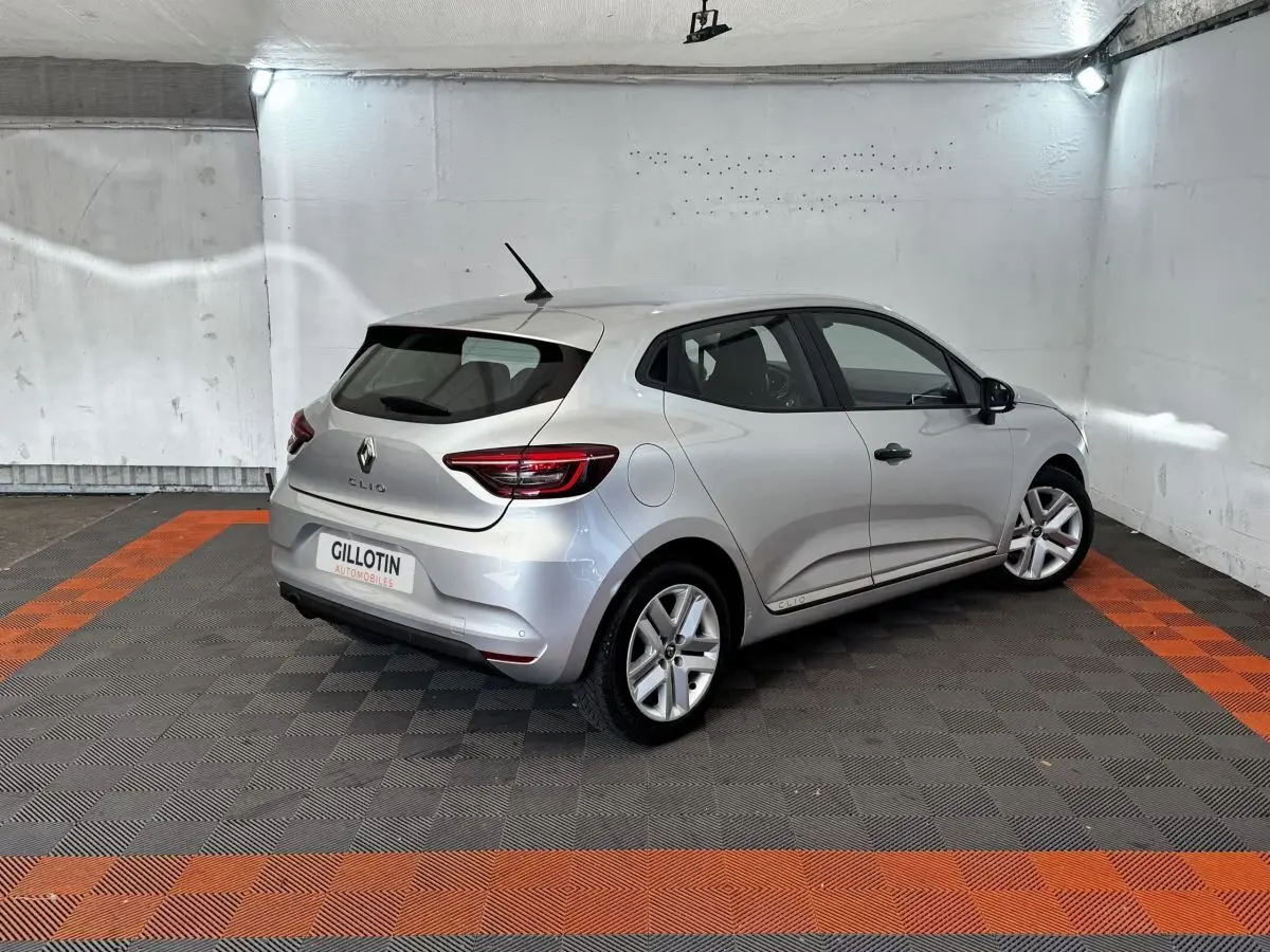 Renault Clio Business TCe 100 gris clair vue 3/4 arrière droit dans un garage avec sol noir et orange.