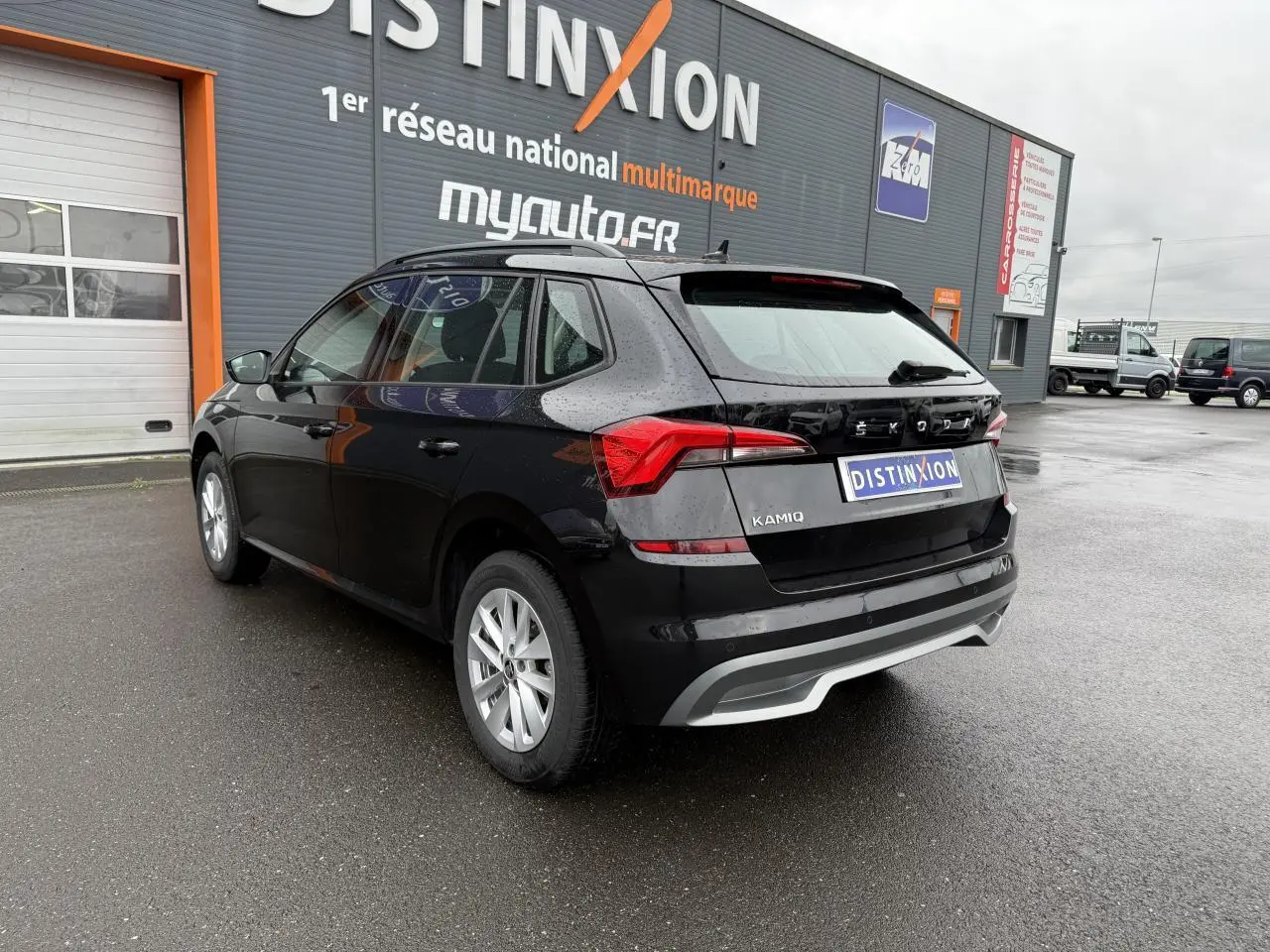 Vue 3/4 arrière droite d'un Skoda Kamiq noir Magic nacré avec feux arrière LED et jantes argentées, stationné devant un bâtiment.