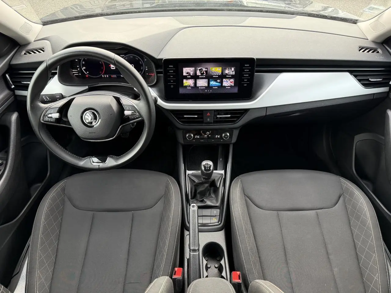 Intérieur du Skoda Kamiq 2023 vu de face, tableau de bord moderne avec écran tactile et sièges tissu noirs.