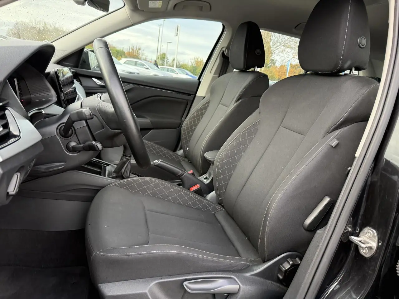 Intérieur du Skoda Kamiq 2023 en vue latérale côté conducteur, sièges tissu noir avec surpiqûres contrastées.