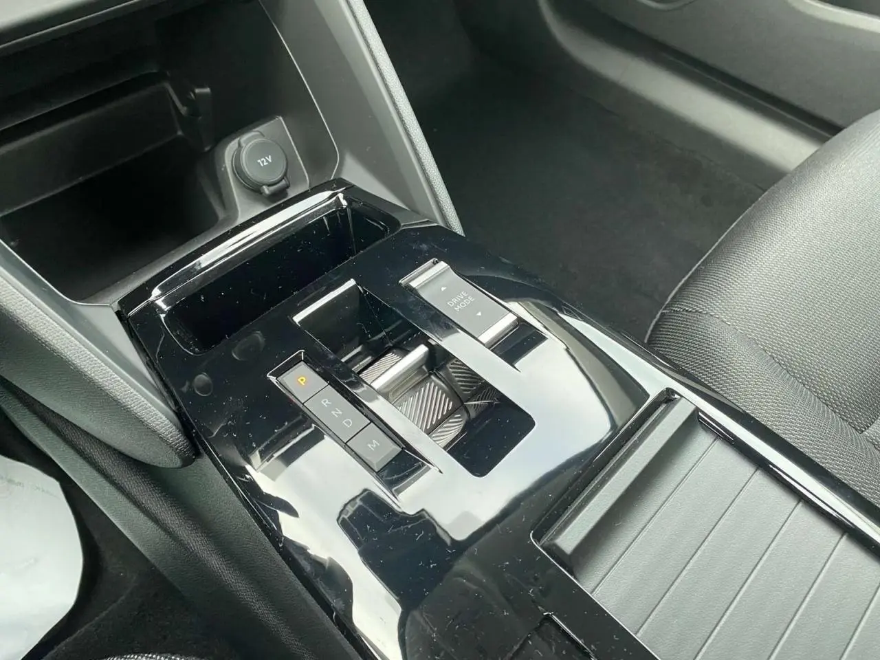Gros plan sur la console centrale noire brillante de la Citroën C4 hybride 2025 avec sélecteur de boîte auto et bouton Drive Mode.