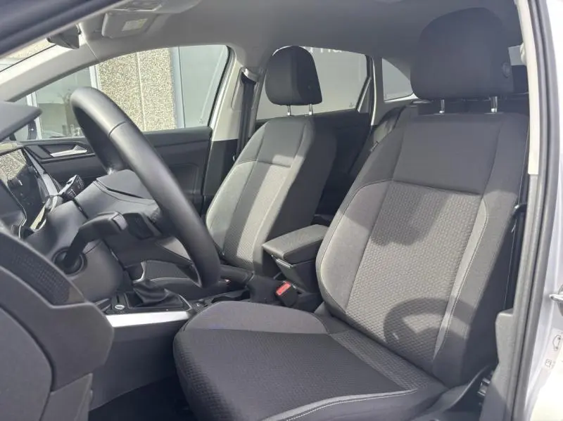 Vue intérieure côté conducteur du Volkswagen Taigo 2025, sièges tissu noir et accoudoir central avec rangement.