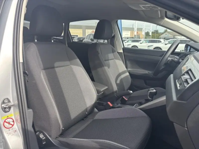 Intérieur avant du Volkswagen Taigo 2025 en Reflet d'Argent, sièges tissu noir et console centrale visible côté gauche.
