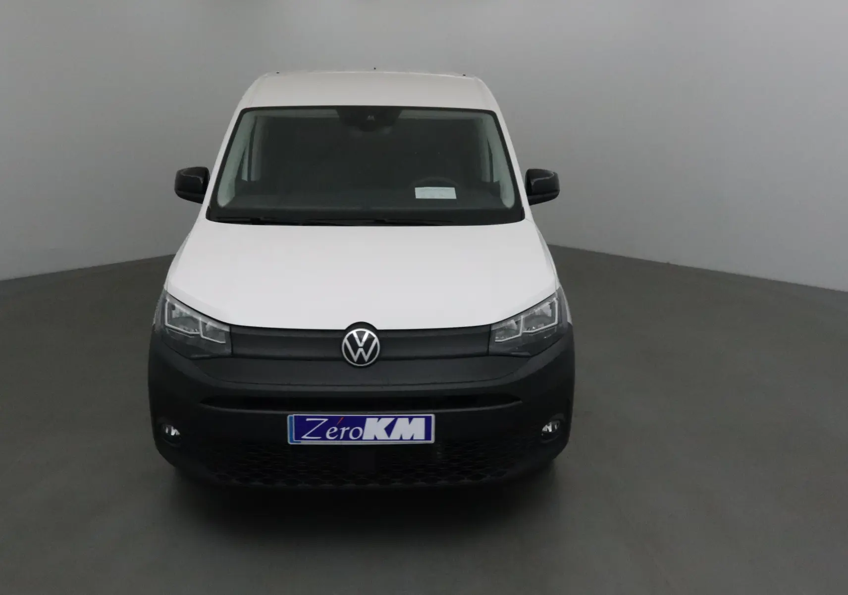 Vue frontale d'un Volkswagen Caddy Maxi blanc avec pare-chocs noir et plaque "Zero KM" visible.