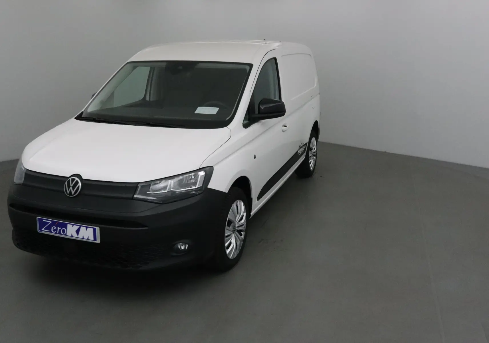 Vue 3/4 avant d'un utilitaire Volkswagen Caddy Maxi blanc avec bouclier noir et jantes argentées.