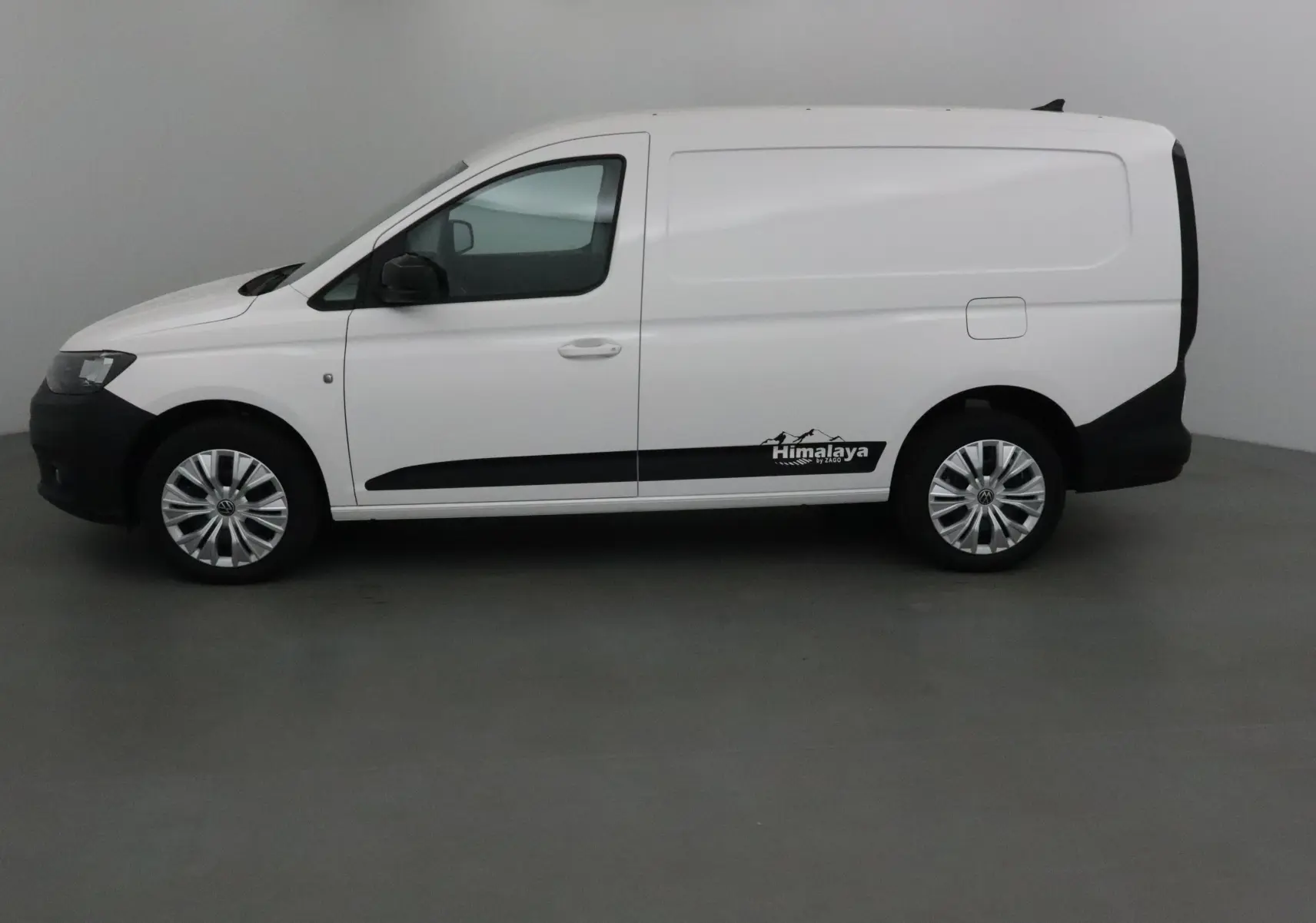 Profil côté gauche d'un utilitaire Volkswagen Caddy Maxi blanc avec bande noire et logo Himalaya sur la porte arrière.