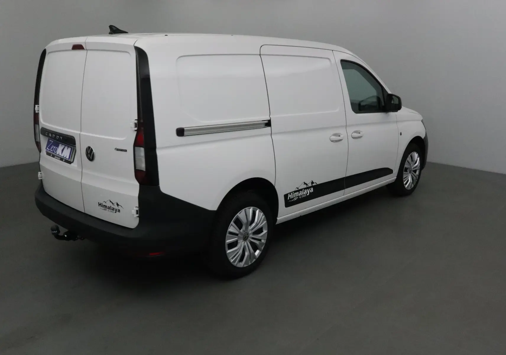 Vue 3/4 arrière droite d'un Volkswagen Caddy Maxi blanc avec logo Himalaya et attelage visible.