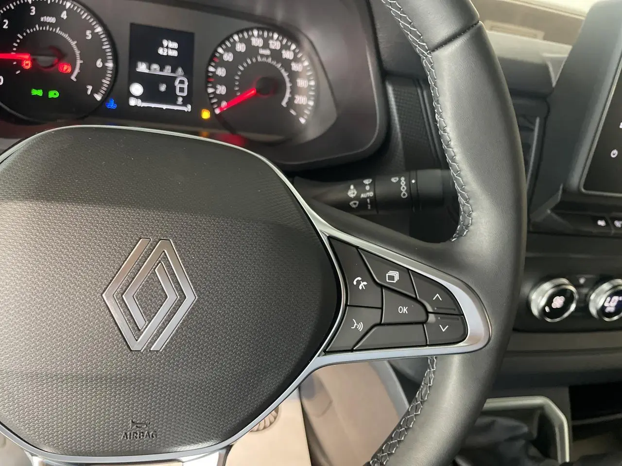 Vue rapprochée du volant noir du Renault Trafic Fourgon avec commandes intégrées et tableau de bord en arrière-plan.