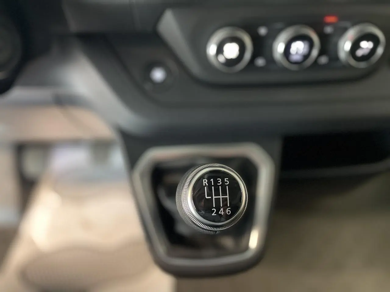 Gros plan sur le levier de vitesses manuel du Renault Trafic Fourgon, avec tableau de bord et commandes de climatisation en arrière-plan.