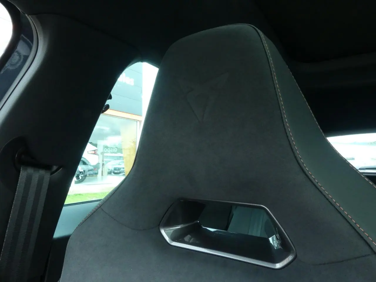 Gros plan sur le siège baquet suédine noir avec surpiqûres cuivrées et logo CUPRA embossé sur l'appuie-tête.