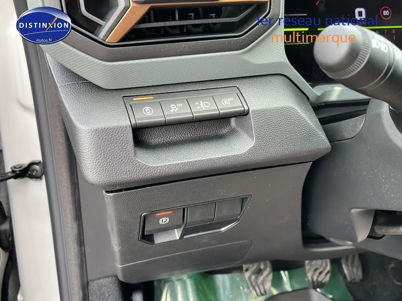 Détail des commandes côté gauche du tableau de bord du Dacia Duster Sandstone 2025, avec boutons d'assistance et frein à main électrique.