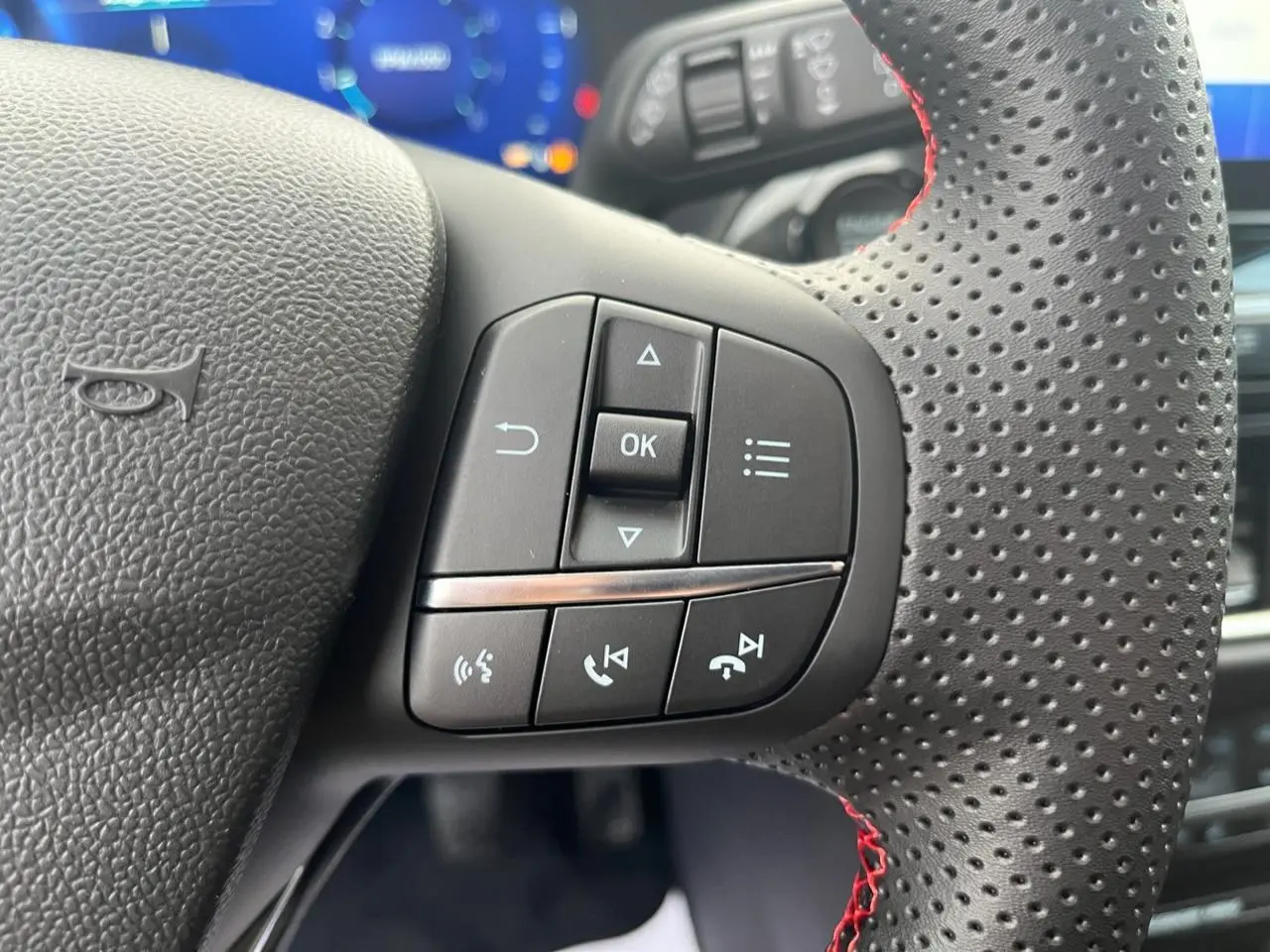 Gros plan sur les commandes multifonctions du volant perforé avec surpiqûres rouges d'un Ford Puma bleu 2022.