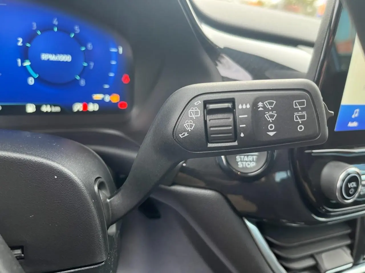 Gros plan sur la commande d'essuie-glace du Ford Puma 2022, avec tableau de bord numérique bleu en arrière-plan.
