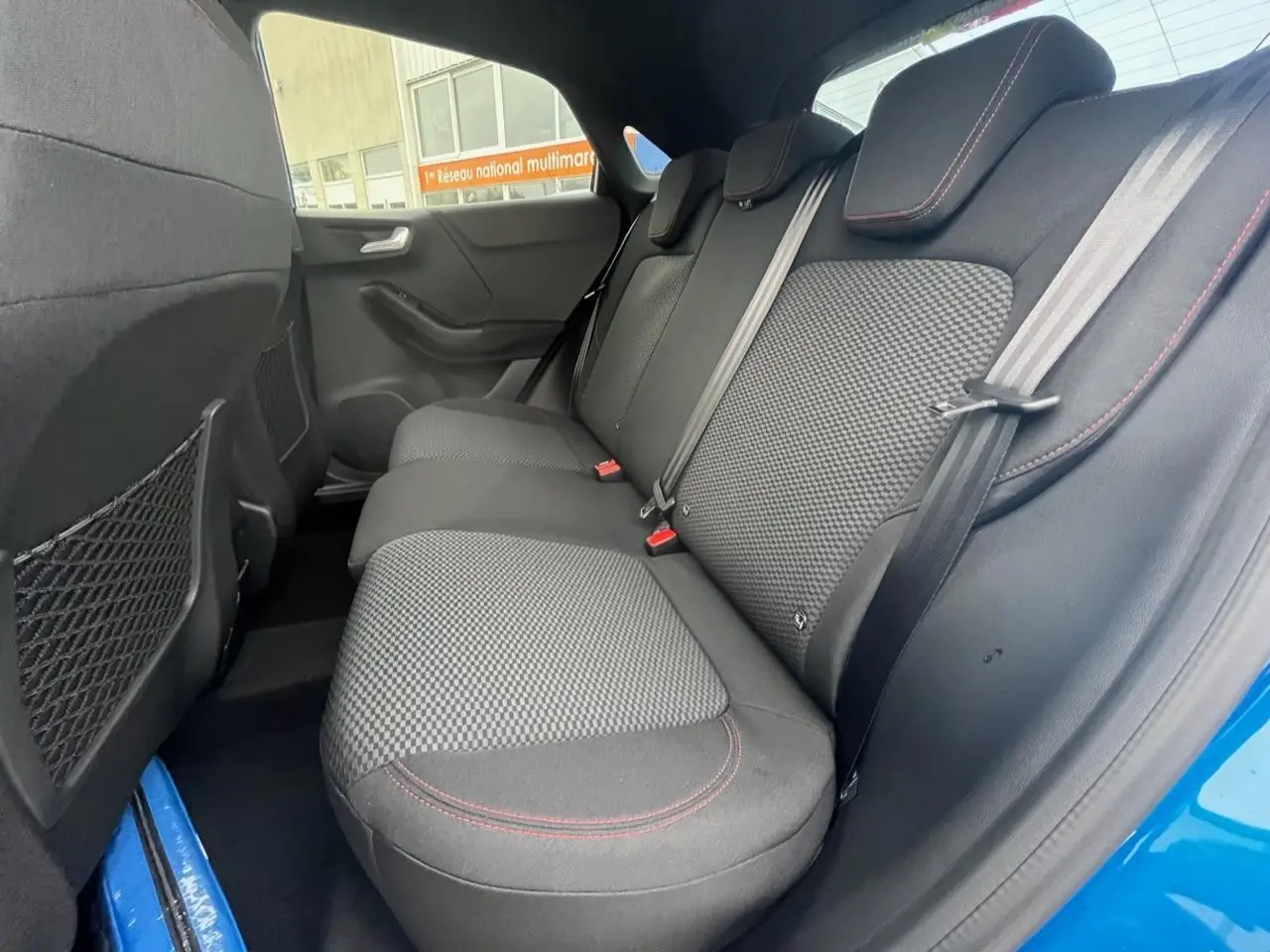 Vue intérieure arrière côté droit du Ford Puma bleu 2022, sièges tissu noir avec surpiqûres rouges.