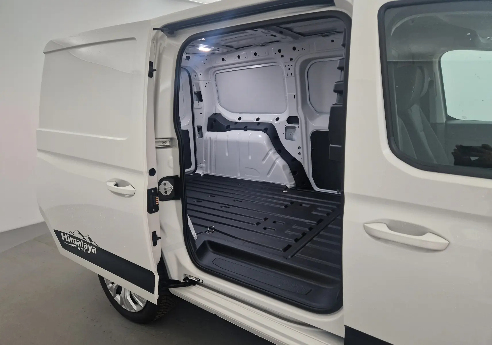 Vue latérale gauche du Volkswagen Caddy Maxi blanc avec porte coulissante ouverte dévoilant l'espace de chargement vide et le logo Himalaya.