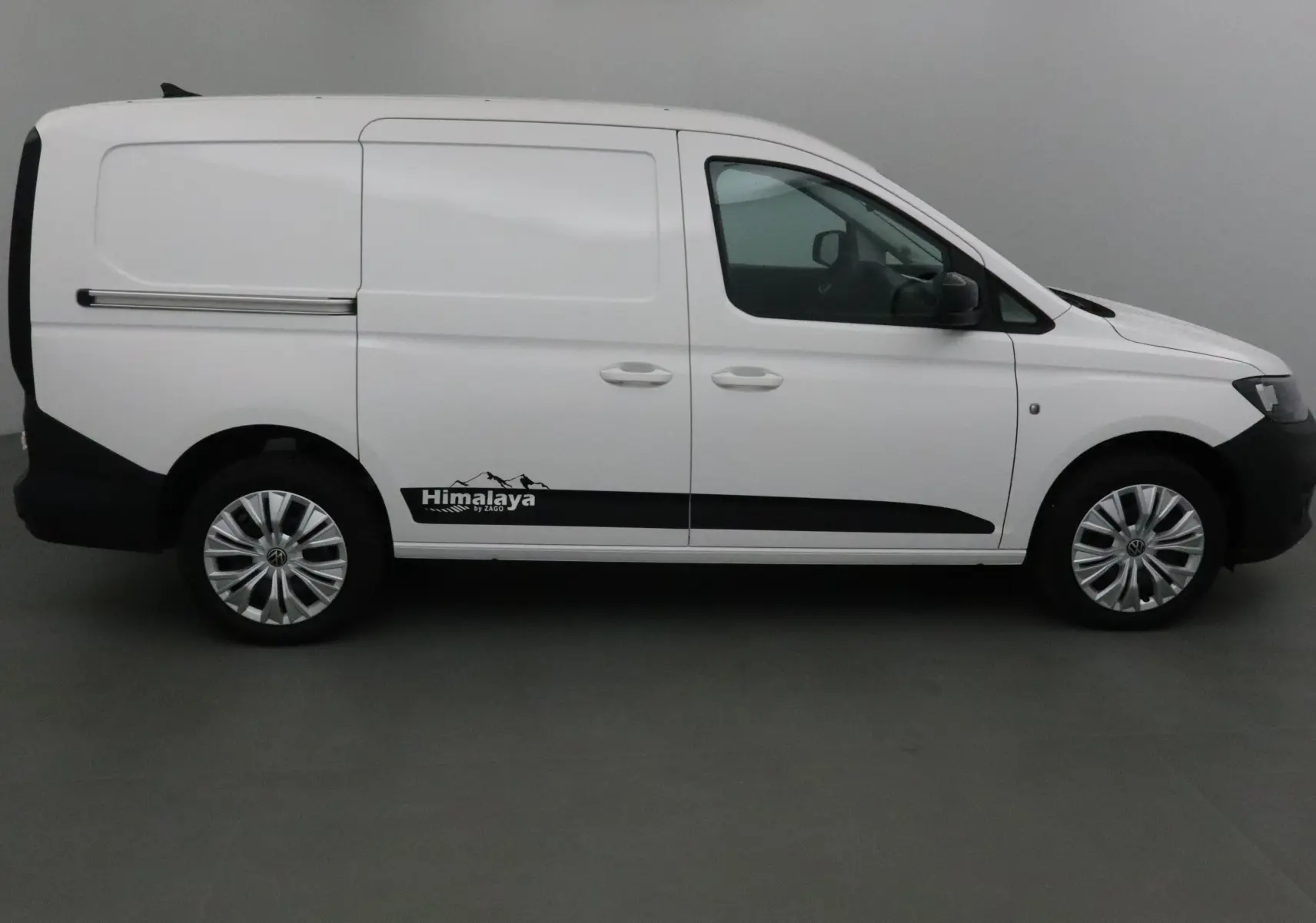 Profil droit d'un Volkswagen Caddy Maxi blanc avec logo Himalaya et jantes argentées dans un studio.