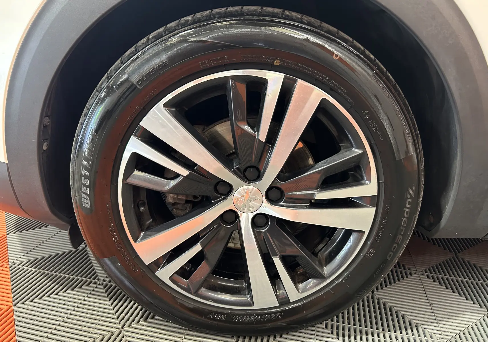 Gros plan sur la roue avant droite d’un Peugeot 3008 blanc, mettant en valeur la jante alliage bicolore et le pneu noir.
