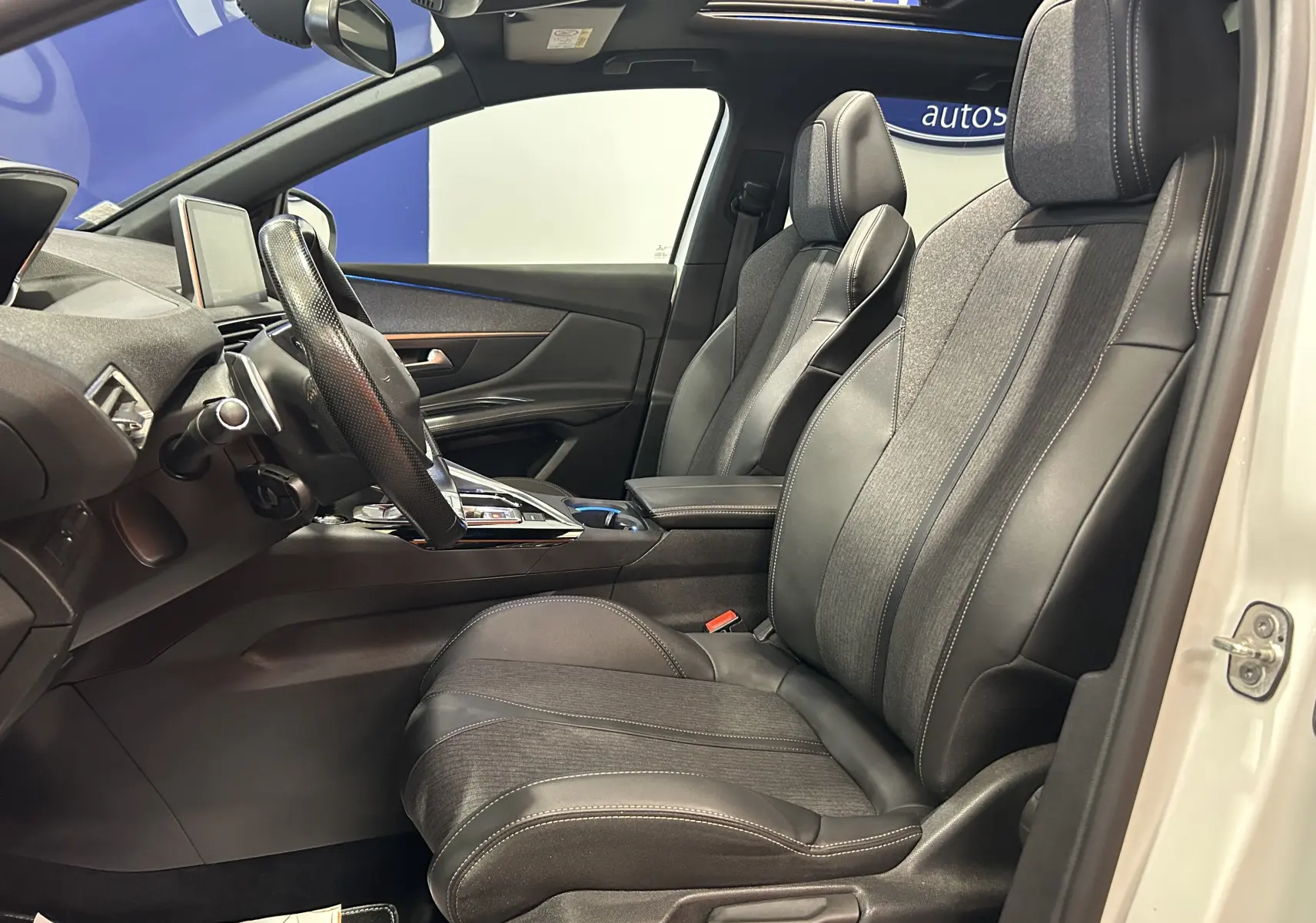 Intérieur côté conducteur du Peugeot 3008 blanc 2020, sièges cuir et tissu, volant multifonction, vue de profil depuis la porte ouverte.