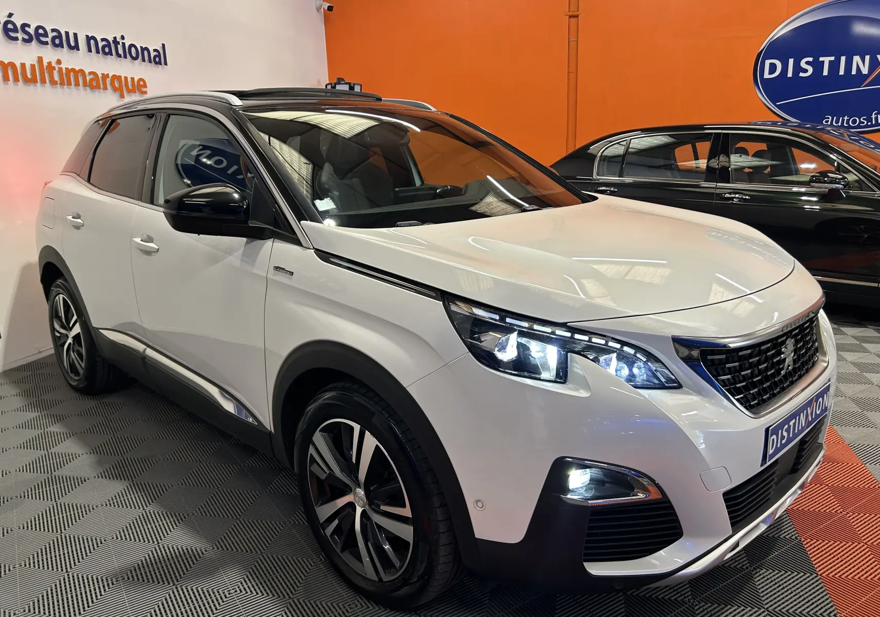 Peugeot 3008 blanc en 3/4 avant droit avec toit ouvrant et phares LED allumés dans un showroom.