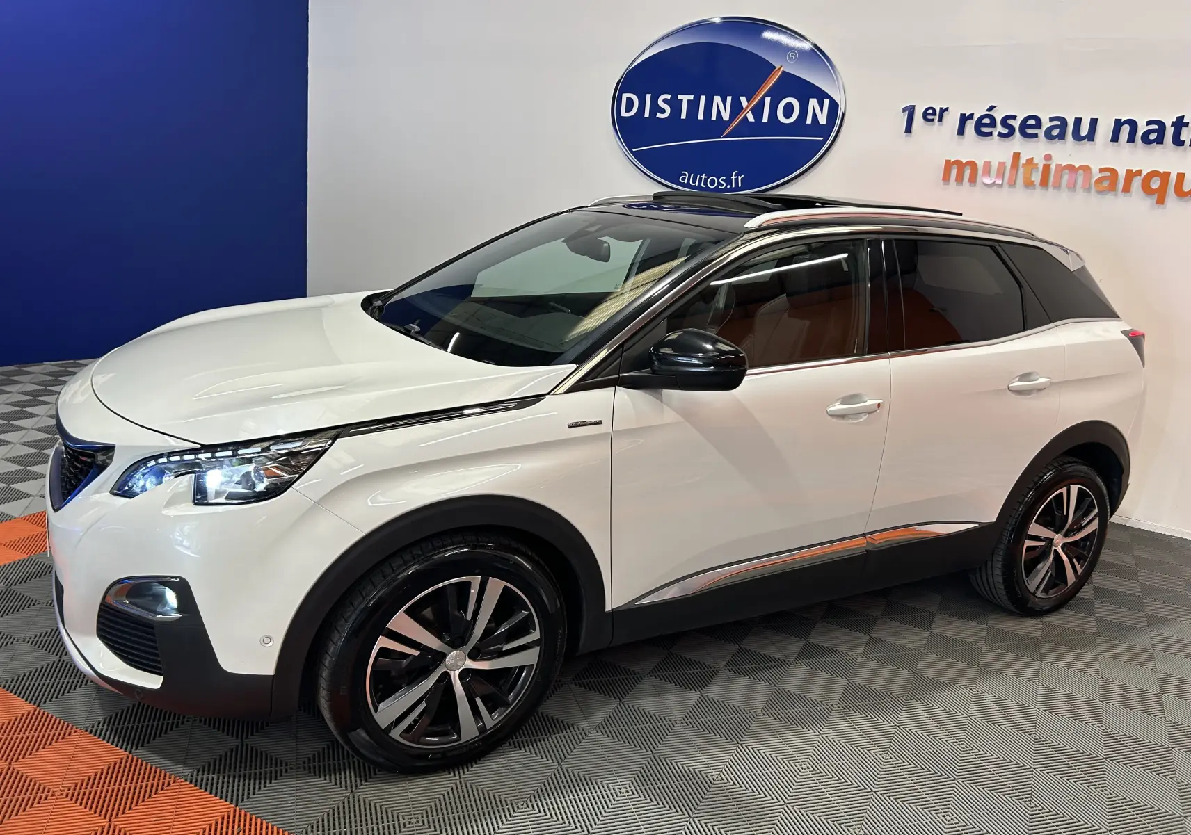 Peugeot 3008 blanc en vue 3/4 avant droit, toit ouvrant et jantes alliage noires visibles en intérieur showroom.