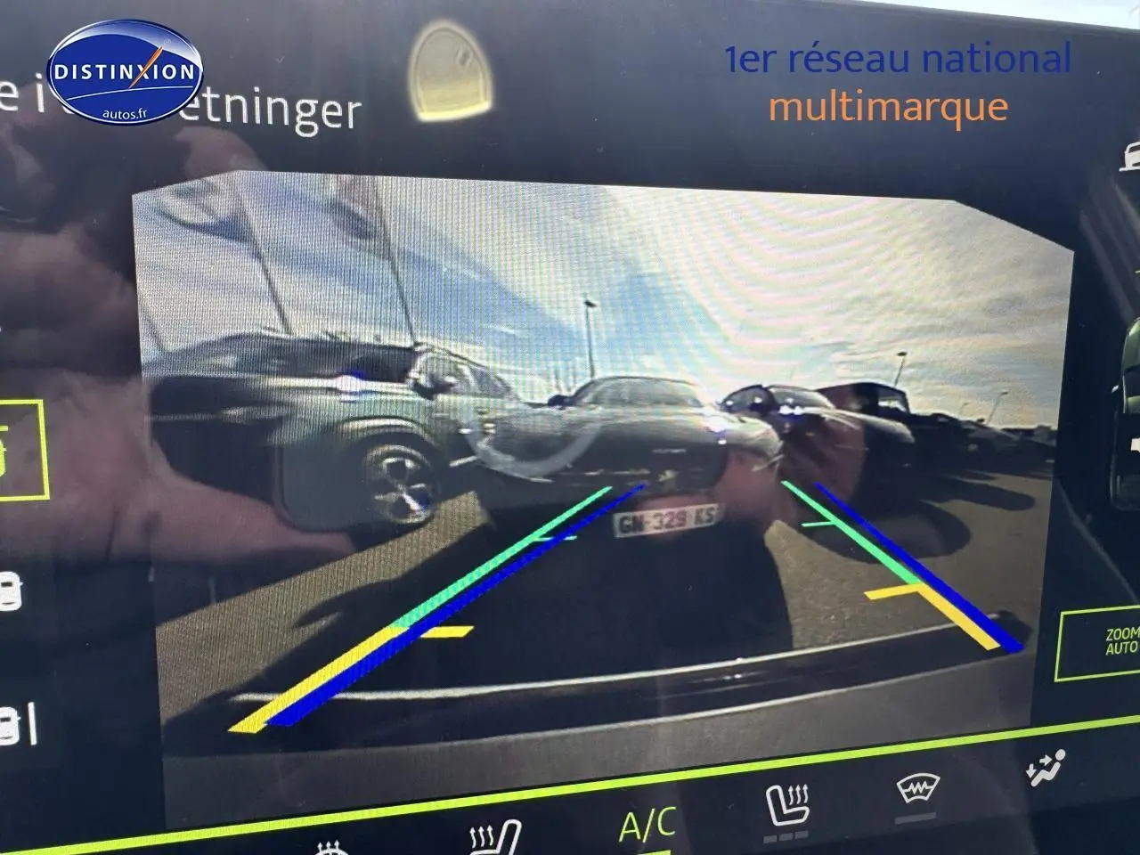 Vue caméra de recul montrant plusieurs véhicules stationnés dont un Dacia Duster vert cèdre à gauche.