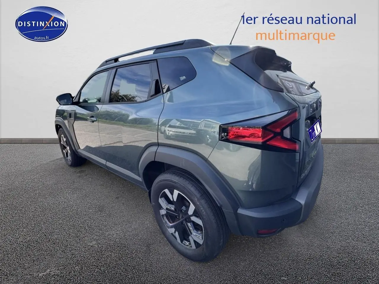 Vue 3/4 arrière droite d'un Dacia Duster 2025 vert cèdre avec barres de toit et jantes alu noires.