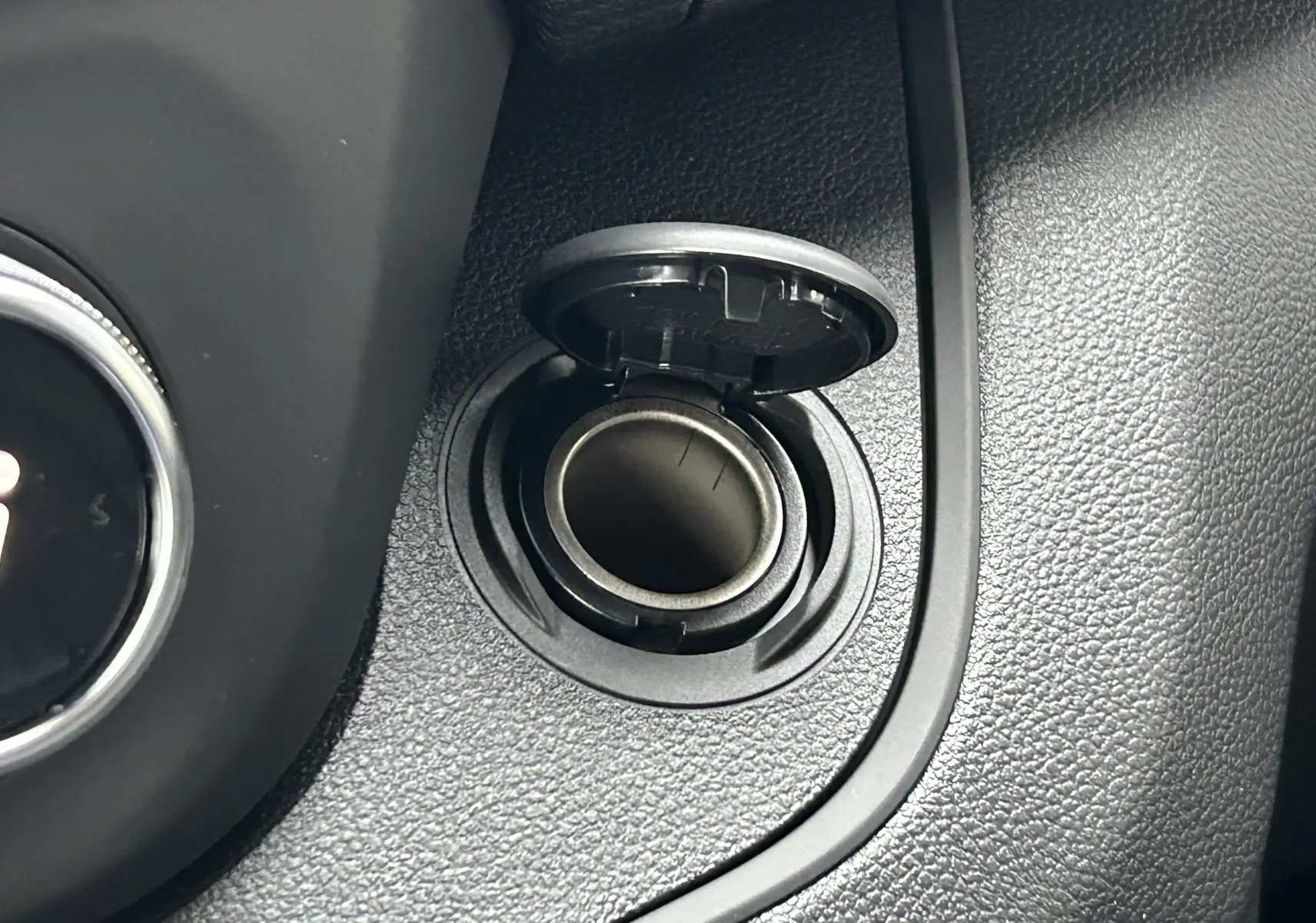 Détail intérieur montrant la prise allume-cigare ouverte sur la console noire du Renault Trafic Fourgon gris Comète.