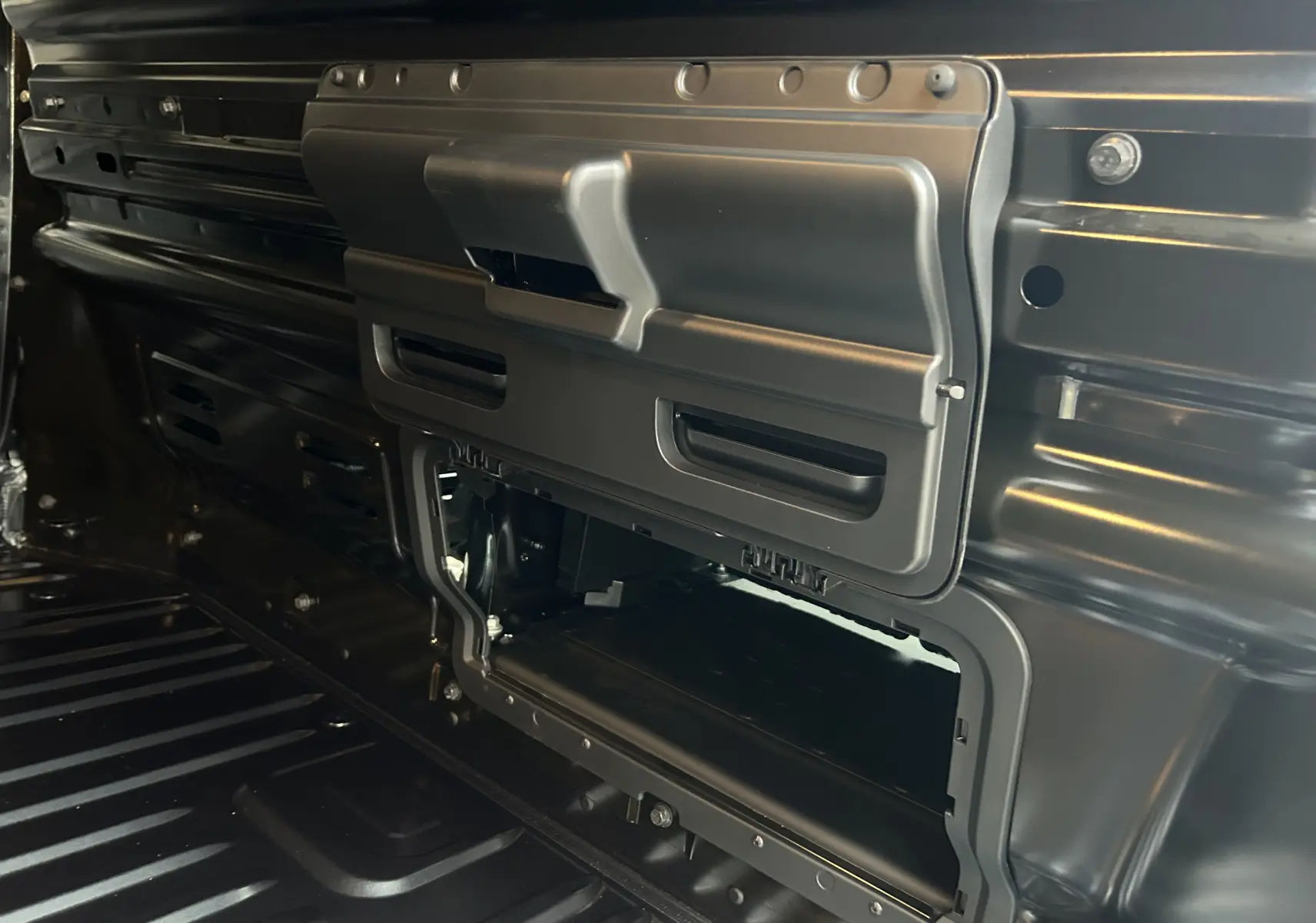 Gros plan intérieur sur la cloison métallique noire du Renault Trafic Fourgon, montrant une trappe de rangement ouverte.