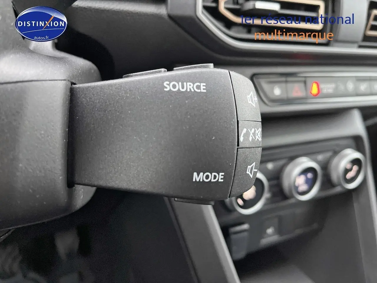 Gros plan sur la commande audio au volant du Dacia Jogger blanc, avec tableau de bord et commandes clim visibles en arrière-plan.