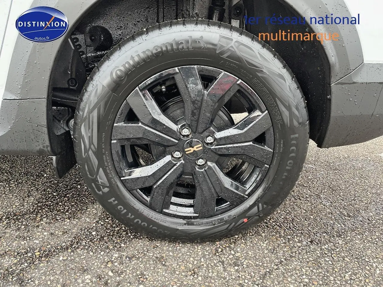 Gros plan sur la roue avant droite avec jante alu noire du Dacia Jogger blanc visible partiellement au-dessus.