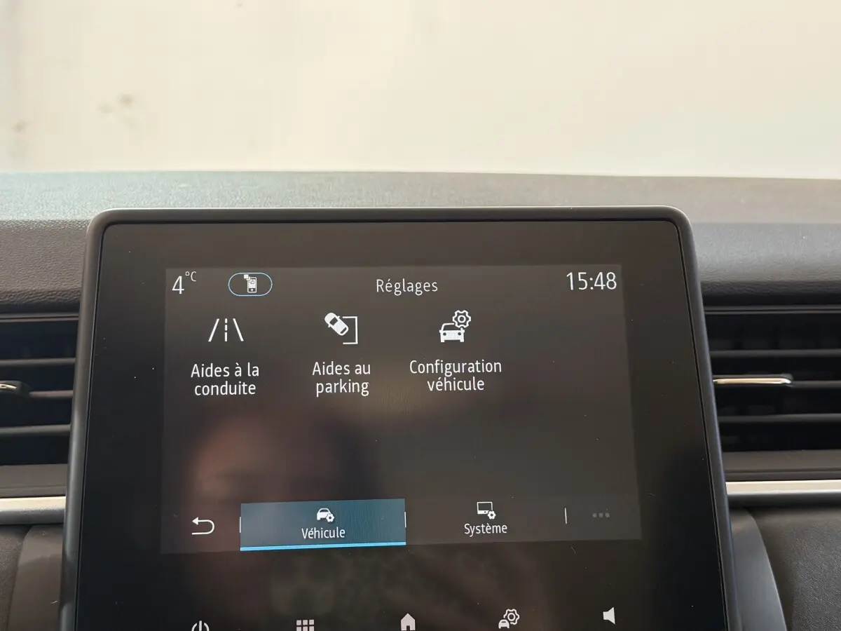 Gros plan sur l'écran tactile central du Renault Captur bleu 2024 affichant les réglages d'aides à la conduite et au parking.