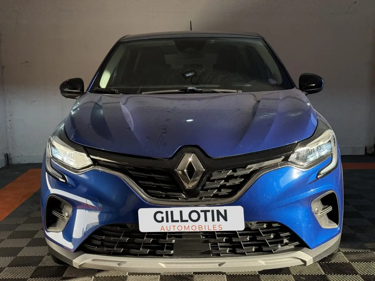 Vue avant d'un Renault Captur bleu 2024 avec calandre noire et phares LED allumés dans un garage.