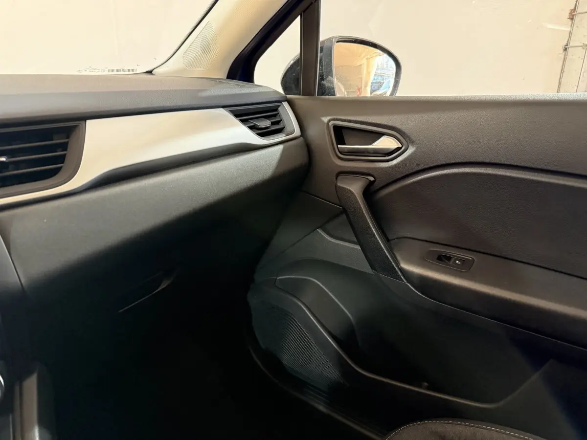 Vue intérieure côté passager du tableau de bord et de la porte noire du Renault Captur bleu, finition Evolution E-Tech 2024.