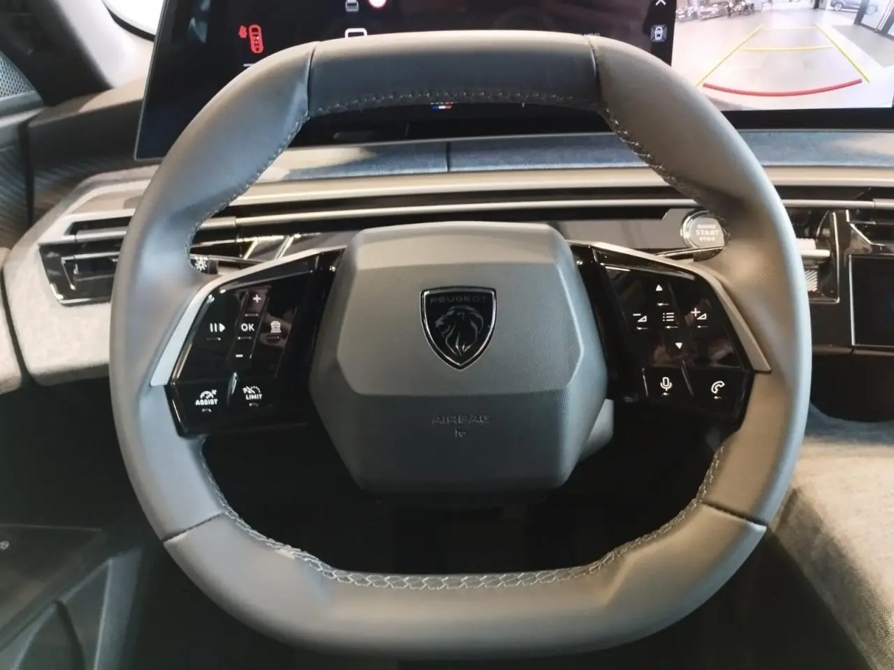 Vue rapprochée du volant gris du Peugeot 3008 2025 avec commandes intégrées et écran incurvé flottant en arrière-plan.