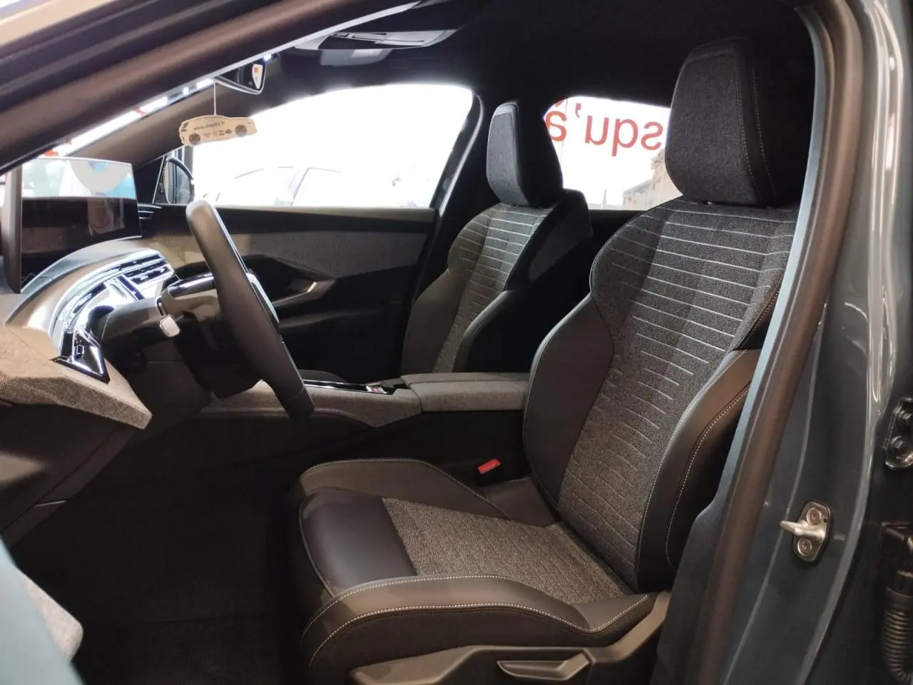 Vue intérieure côté conducteur du Peugeot 3008 2025 avec sièges tissu gris et cuir noir, planche de bord moderne et écran flottant.