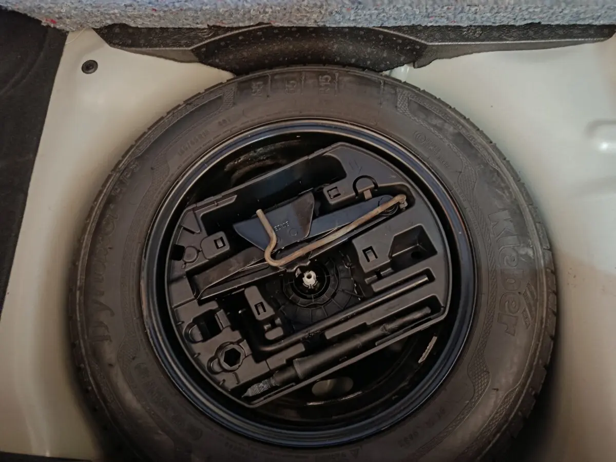 Vue plongeante sur la roue de secours noire et ses outils intégrés dans le coffre blanc d'une Citroën C3 2020.
