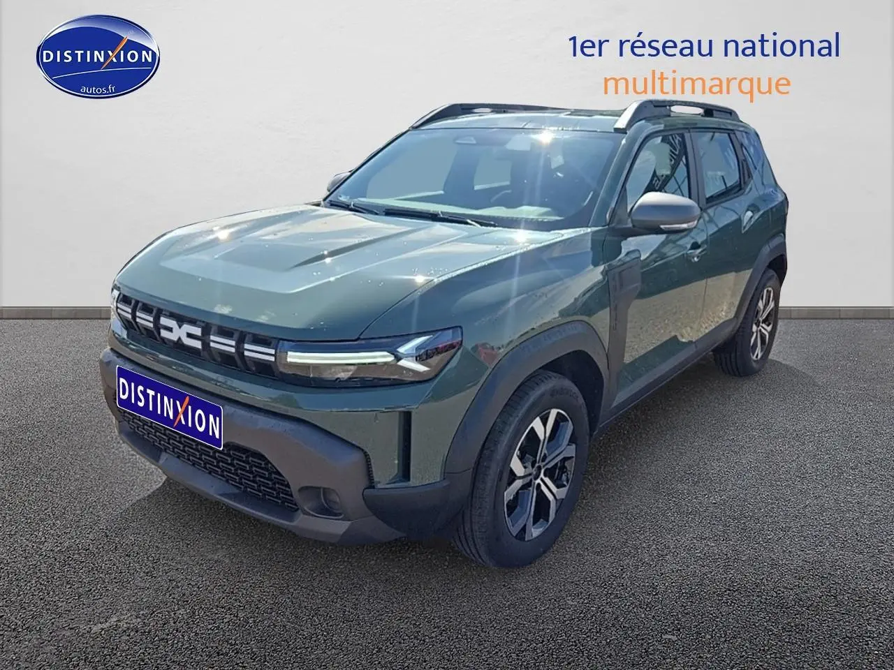 SUV Dacia Duster vert kaki en 3/4 avant droit avec jantes alu et barres de toit visibles.