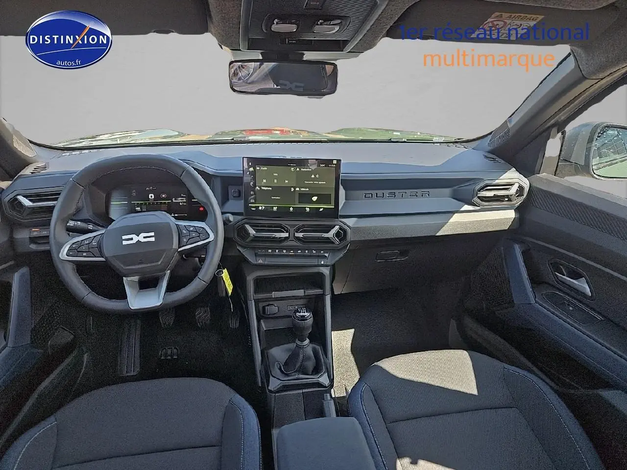 Vue intérieure avant du Dacia Duster 2025 montrant le volant multifonction, écran tactile et levier de vitesses manuel.
