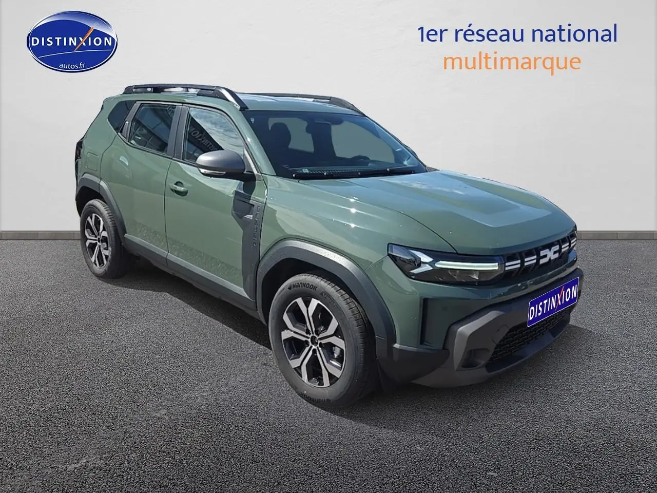 Vue 3/4 avant gauche du Dacia Duster 2025 vert kaki avec barres de toit et jantes alu noires et argentées.
