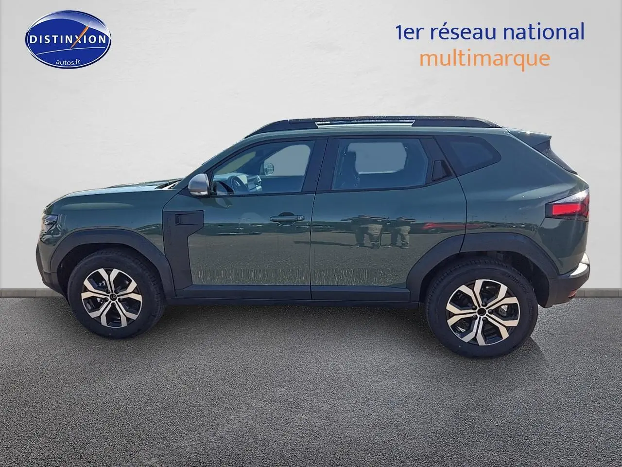 Profil droit du Dacia Duster vert kaki 2025 avec jantes alu et barres de toit visibles sur fond clair.