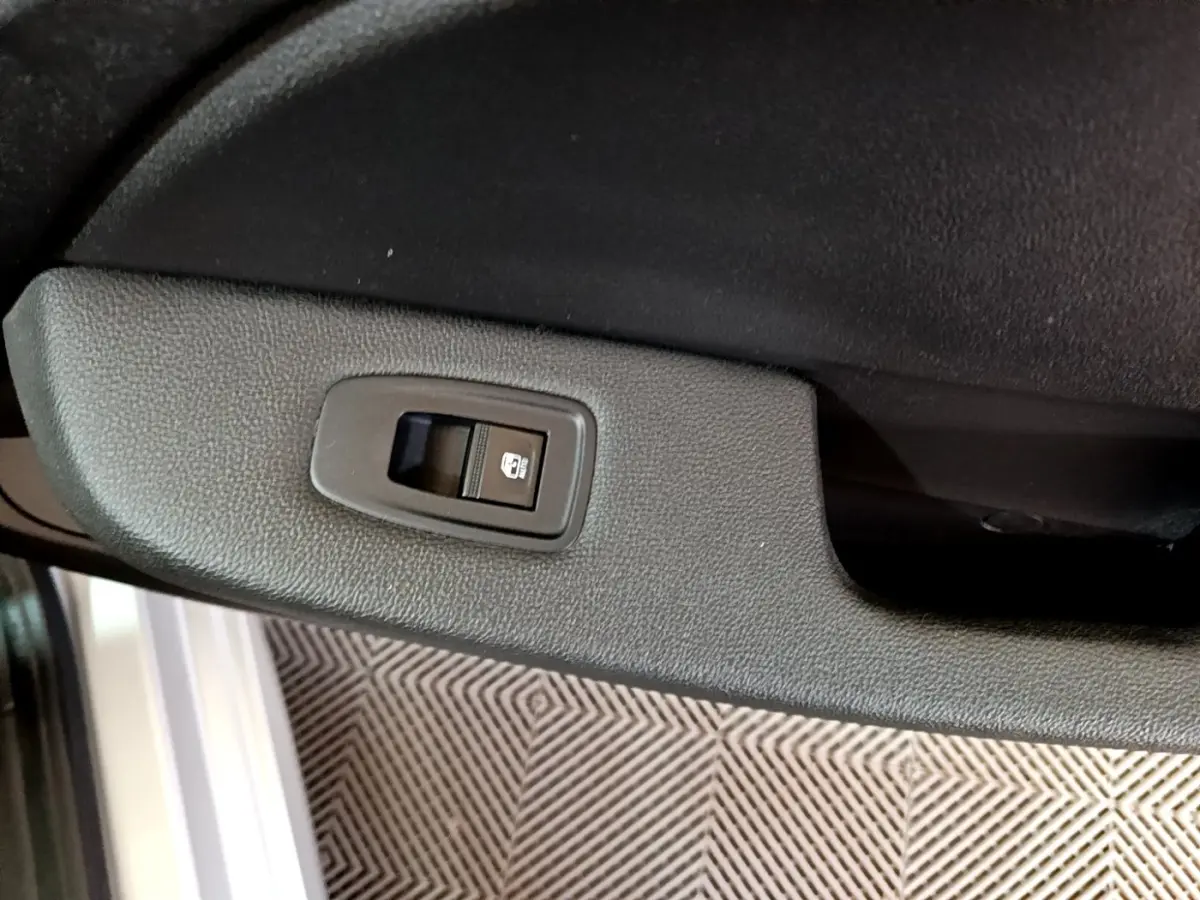 Détail de l'interrupteur de lève-vitre arrière sur la porte intérieure noire d'une Renault Clio Business E-TECH 140 gris foncé.