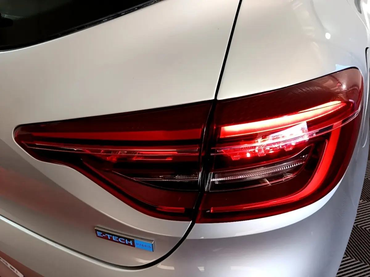 Gros plan sur le feu arrière droit rouge et le badge E-TECH sur la carrosserie gris clair d'une Renault Clio.