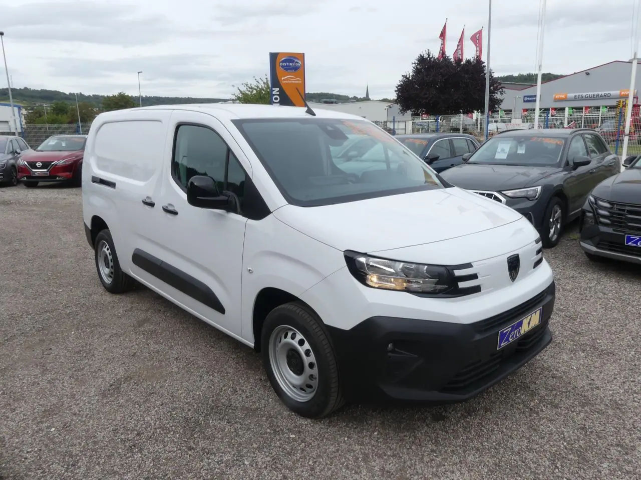 Peugeot Partner blanc en 3/4 avant droit, avec boucliers noirs et jantes tôles grises, stationné en extérieur.