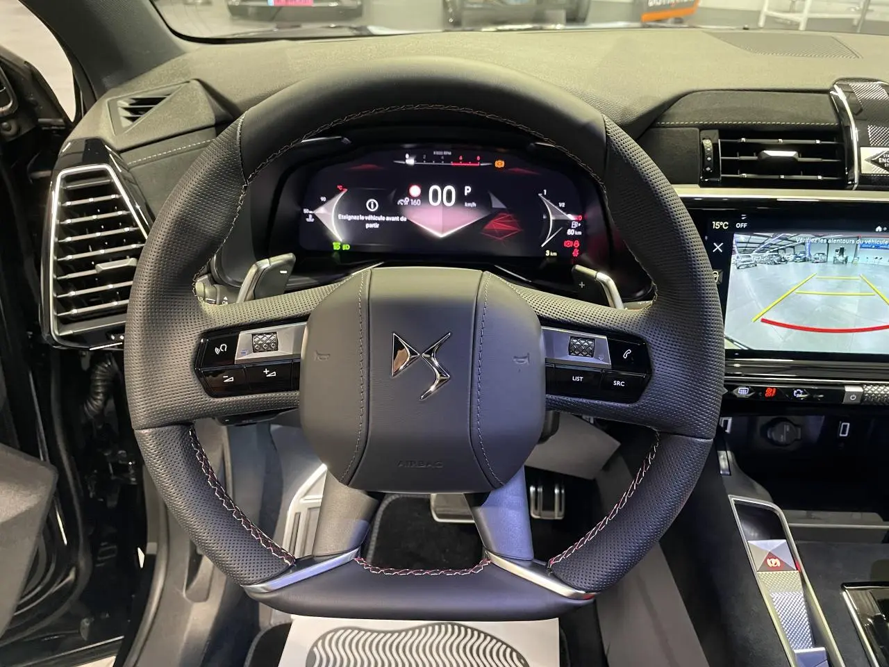 Vue intérieure centrée sur le volant DS en cuir perforé avec surpiqûres carmin et or du DS7 Crossback noir métallisé.