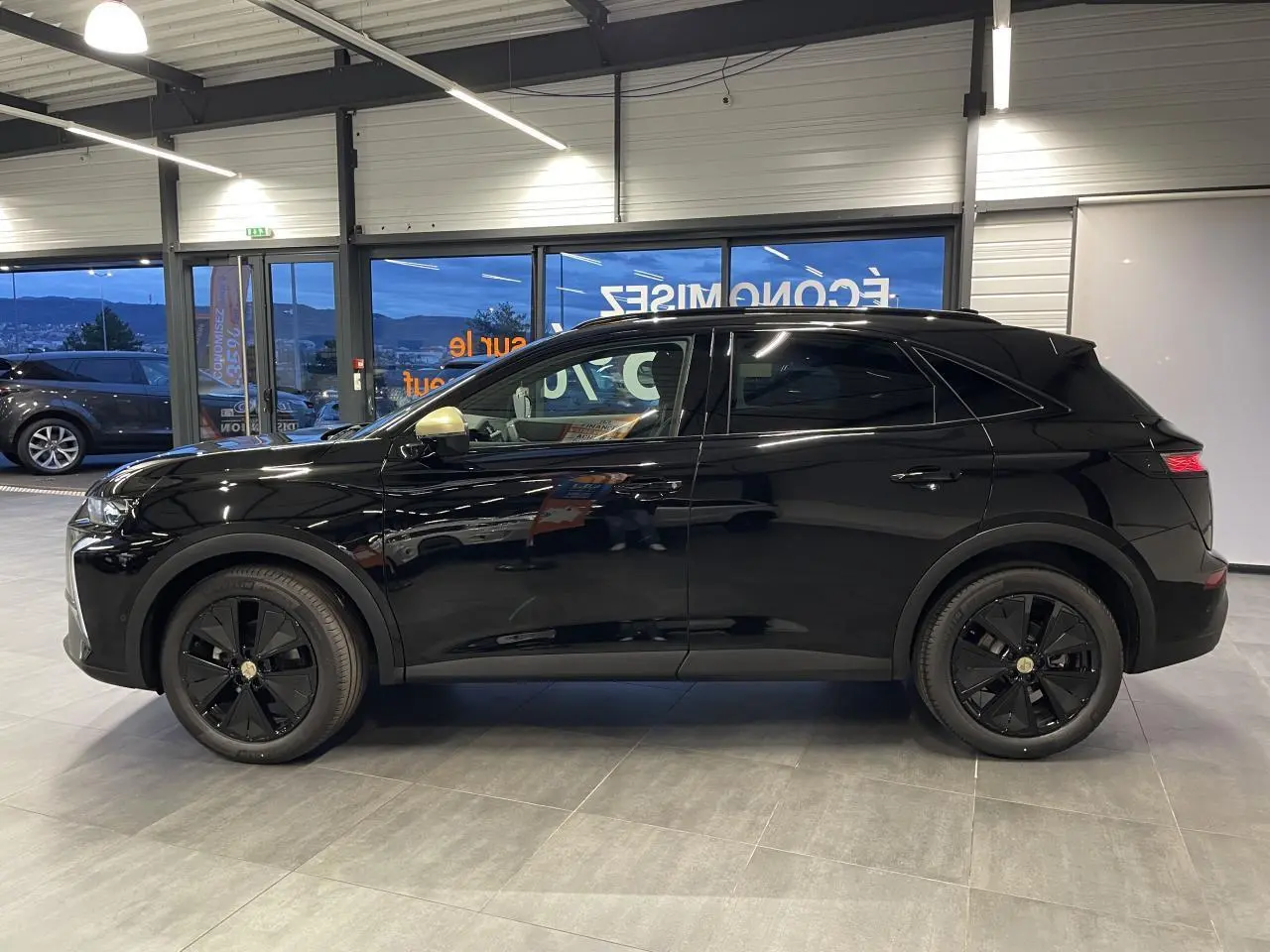 Vue de profil côté gauche du DS7 Crossback noir métallisé avec jantes noires et calandre discrète en intérieur showroom.