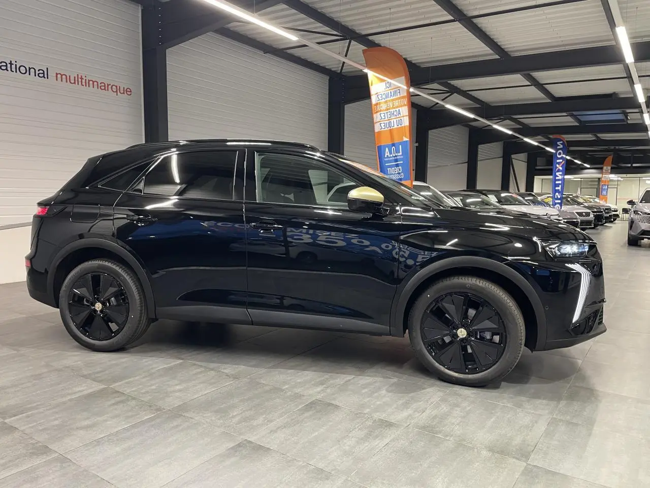 Vue de profil droit du DS7 Crossback noir métallisé avec coques de rétroviseurs dorées satinées en intérieur showroom.