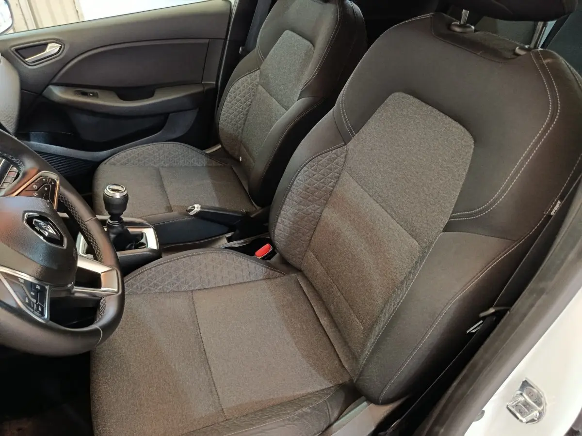 Vue intérieure côté conducteur de la Renault Clio Business blanche 2021, sièges tissu gris et volant cuir multifonctions.