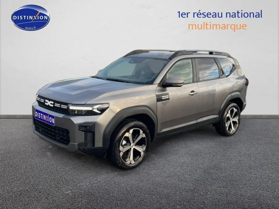 Vue 3/4 avant d'un Dacia Bigster gris schiste métal avec jantes alliage et barres de toit noires.