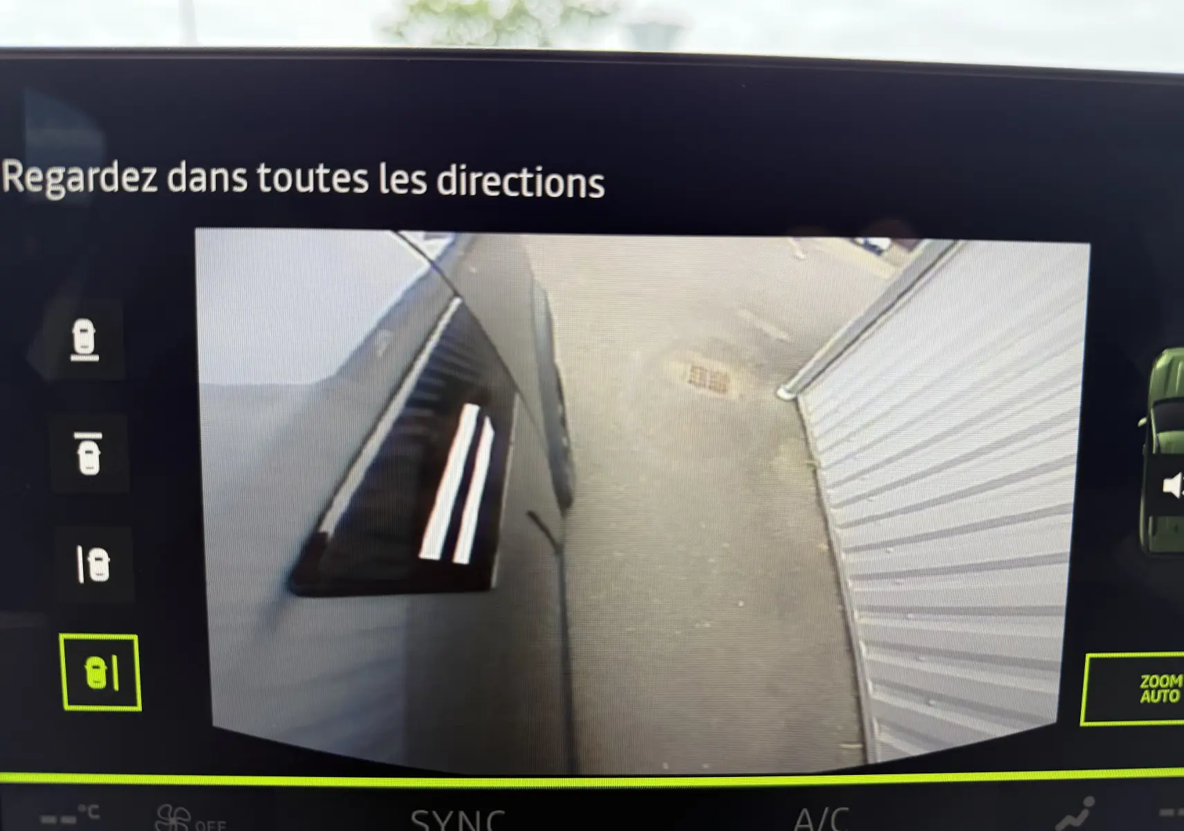 Vue caméra latérale gauche du Dacia Bigster gris schiste métal, montrant la porte et le sol à côté d'un mur blanc.