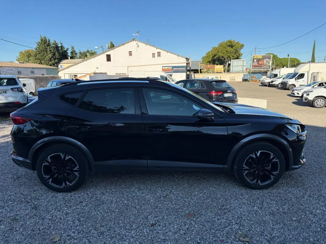 Profil latéral gauche d'un CUPRA Formentor noir 2024, SUV hybride avec jantes noires au design sportif, sur parking extérieur.